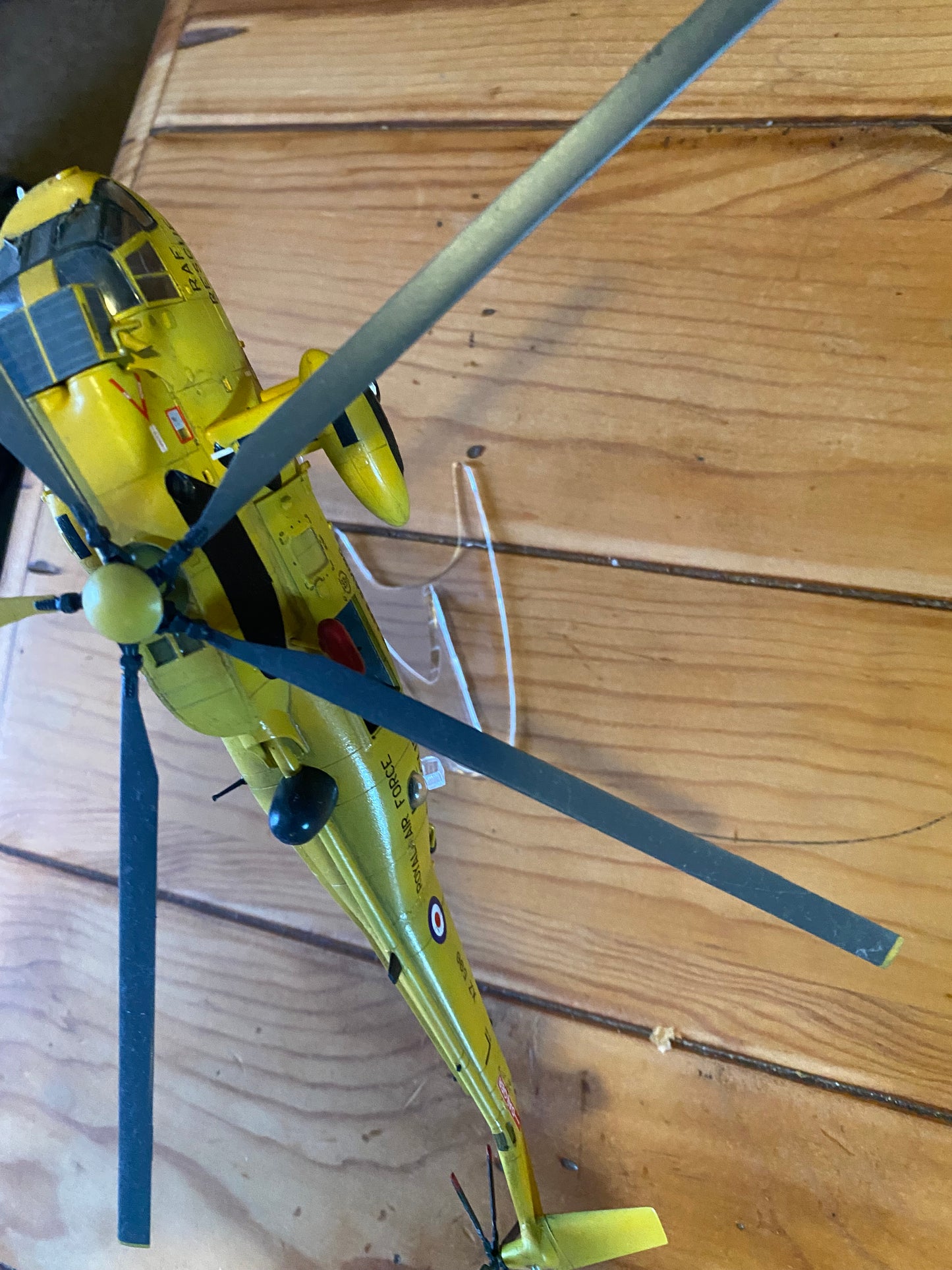 Yellow RAF rescue helicopter model mounted on a clear, U-shaped acrylic display stand on a wooden surface.