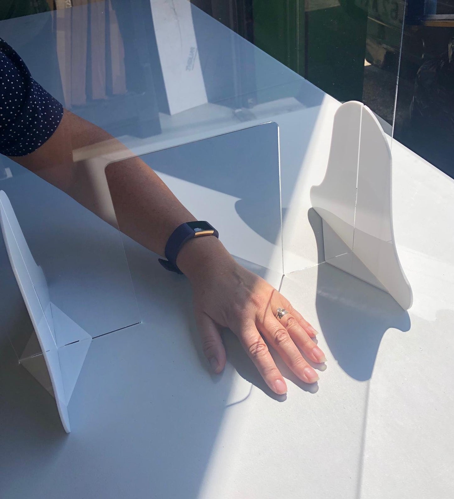 Clear acrylic SuperCoolCreations sneeze guard with curved white plastic support stands on a white surface.