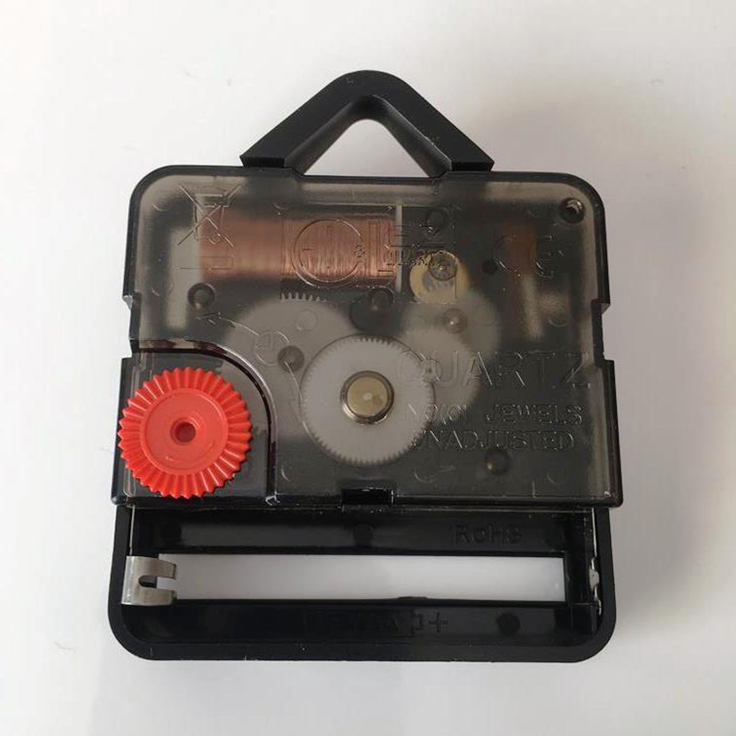 Black quartz clock movement mechanism with a small red adjustment gear and transparent cover on a white background.