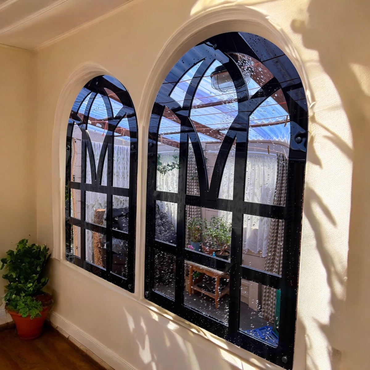 Pair of black Victorian arch garden mirrors mounted on a beige wall, reflecting an outdoor patio.