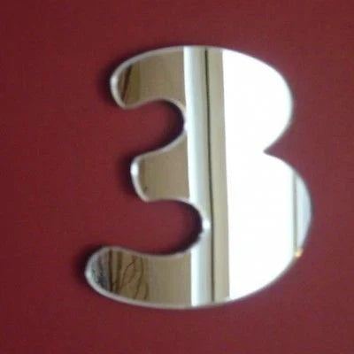 A reflective mirror shaped like the number 3, mounted on a solid dark red wall.