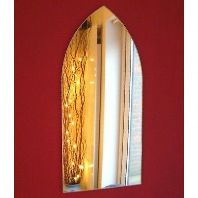 Gothic arch-shaped wall mirror hanging on a solid red wall, reflecting a lit twig lamp and a window.
