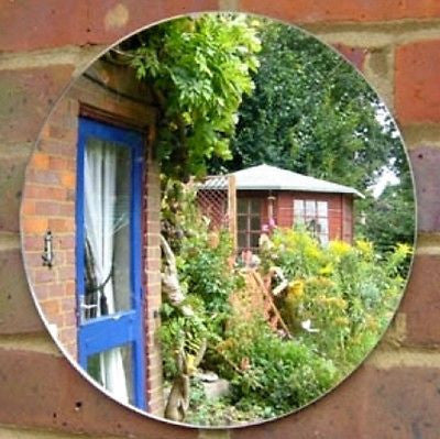 A round garden mirror mounted on a brick wall, reflecting a garden, trees, and a shed.