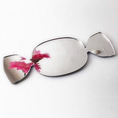 Candy-shaped silver mirror reflecting pink flowers on a white surface.