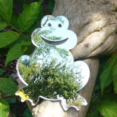 A smiling frog-shaped mirror resting on a tree branch, reflecting trees.