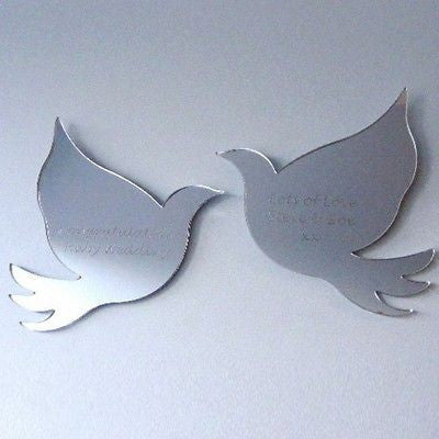 A pair of reflective dove-shaped acrylic mirrors with engraved text, mounted on a wall.