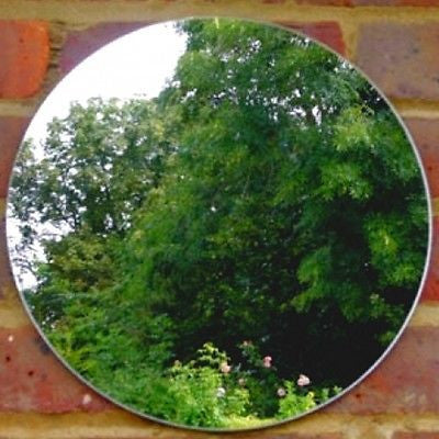 Round garden mirror mounted on a red brick wall, reflecting green trees and foliage.