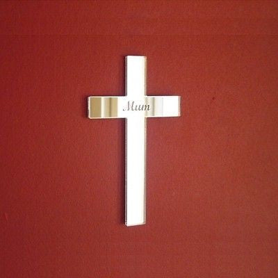 A cross-shaped acrylic mirror engraved with the word Mum, mounted on a solid red wall.