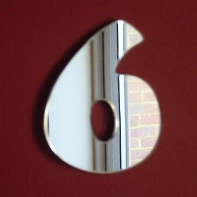 A silver mirror shaped like the number 6 mounted on a dark red wall.