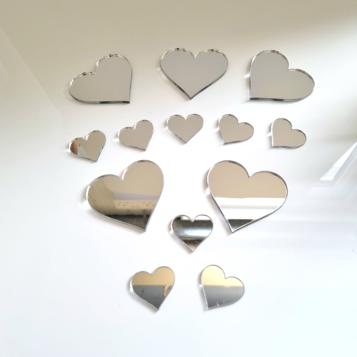 A bundle of thirteen heart-shaped silver mirrors in various sizes arranged on a white surface.
