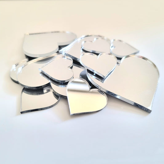 A pile of assorted silver heart-shaped mirrors in various sizes on a white surface.