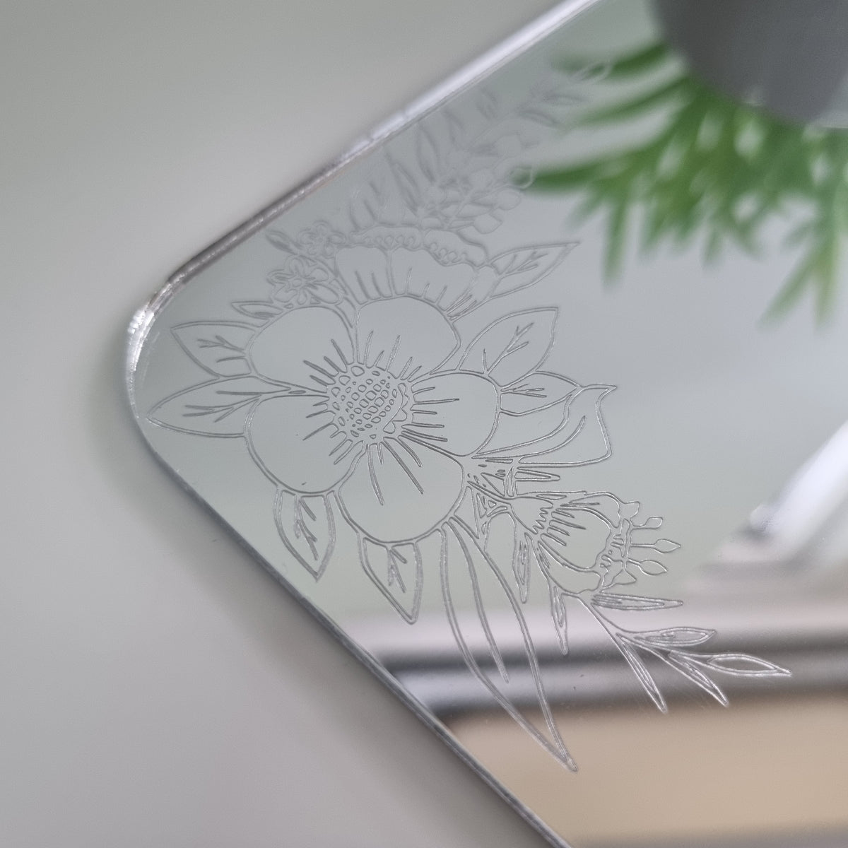 Close-up of a rectangular mirror featuring a delicate floral etched design with flowers and leaves on its surface.