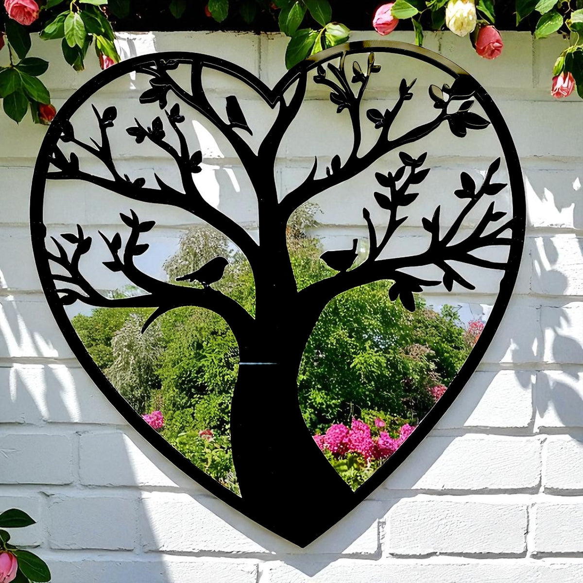 Heart-shaped garden mirror featuring a black metal Tree of Life silhouette with birds on branches.