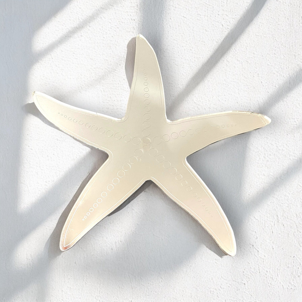 Etched starfish-shaped mirror mounted on a white textured wall.
