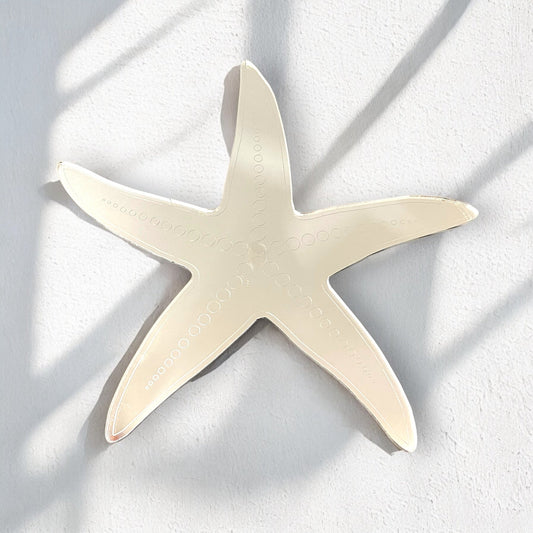Etched starfish-shaped mirror mounted on a white textured wall.