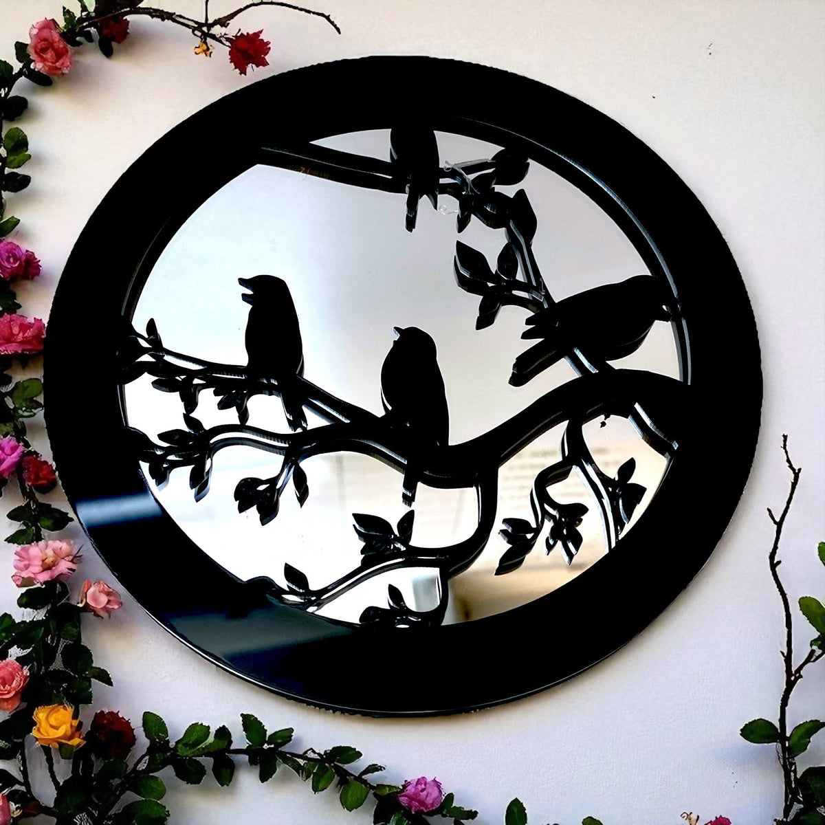 Round black garden mirror with a black silhouette design of birds sitting on tree branches.