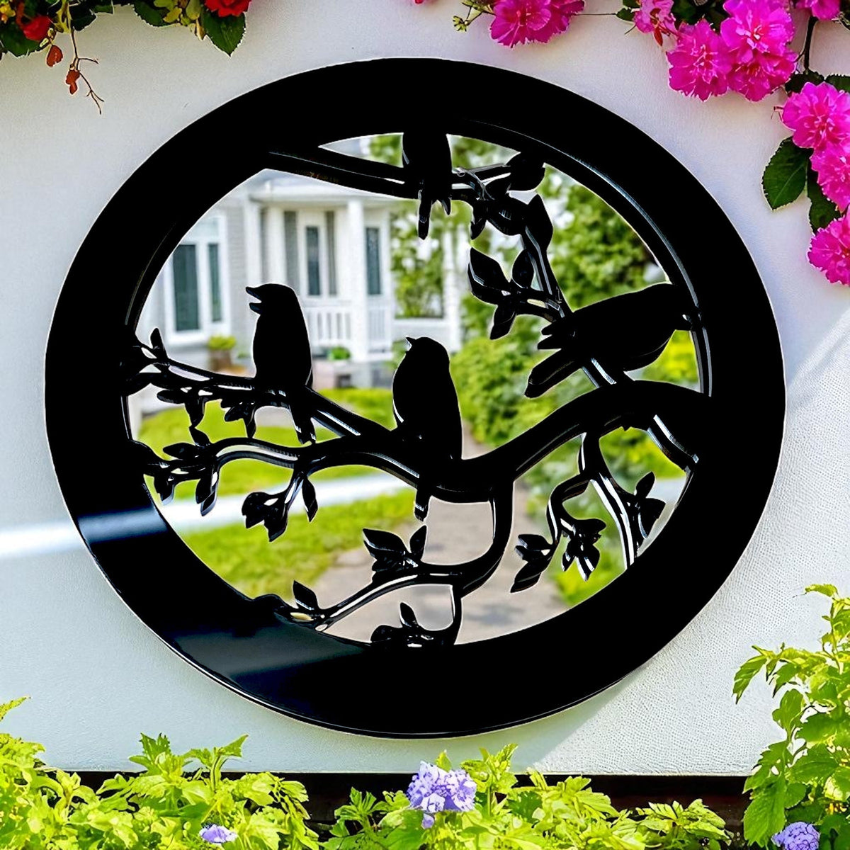 Round black garden mirror with a cutout silhouette of birds perched on leafy branches.