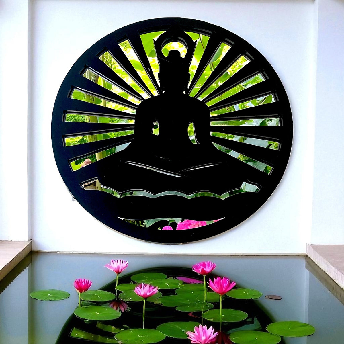 Round black Buddha garden mirror mounted on a white wall above a pond with pink lotus flowers.