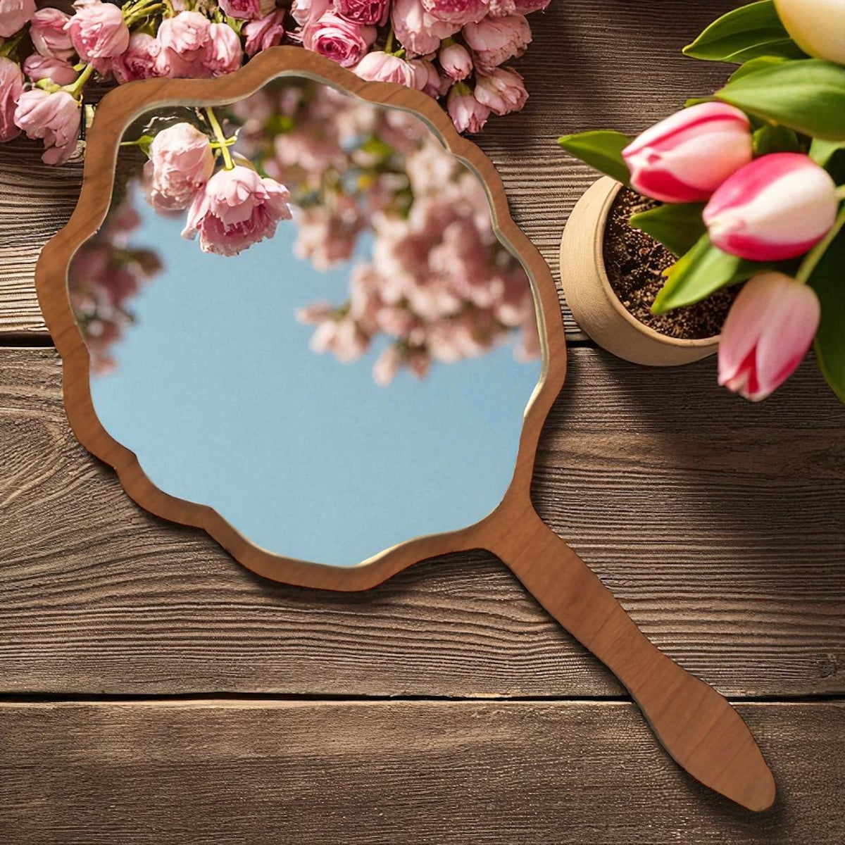 Scalloped wooden hand mirror on a dark wooden surface with pink flowers and tulips.