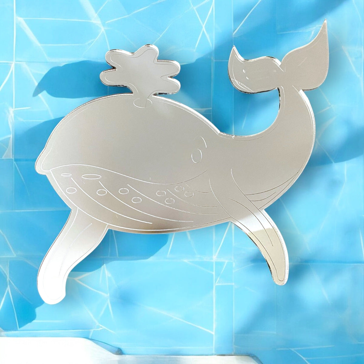 Silver etched whale-shaped mirror on a blue cracked background.