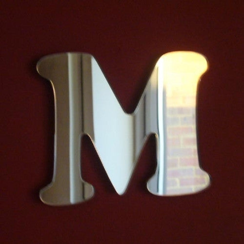 A mirror shaped like a stylized letter M, with a reflective surface mounted on a dark red wall.
