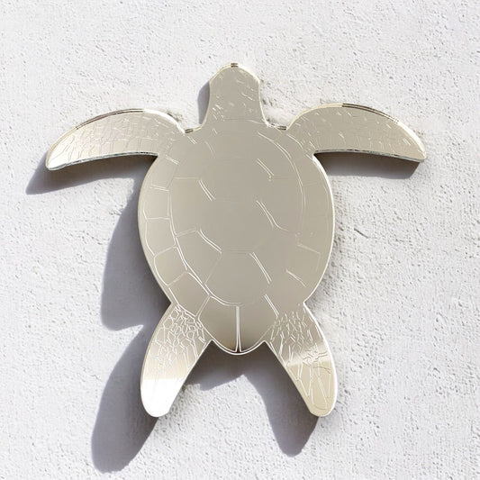 An etched silver turtle-shaped mirror mounted on a white textured wall.