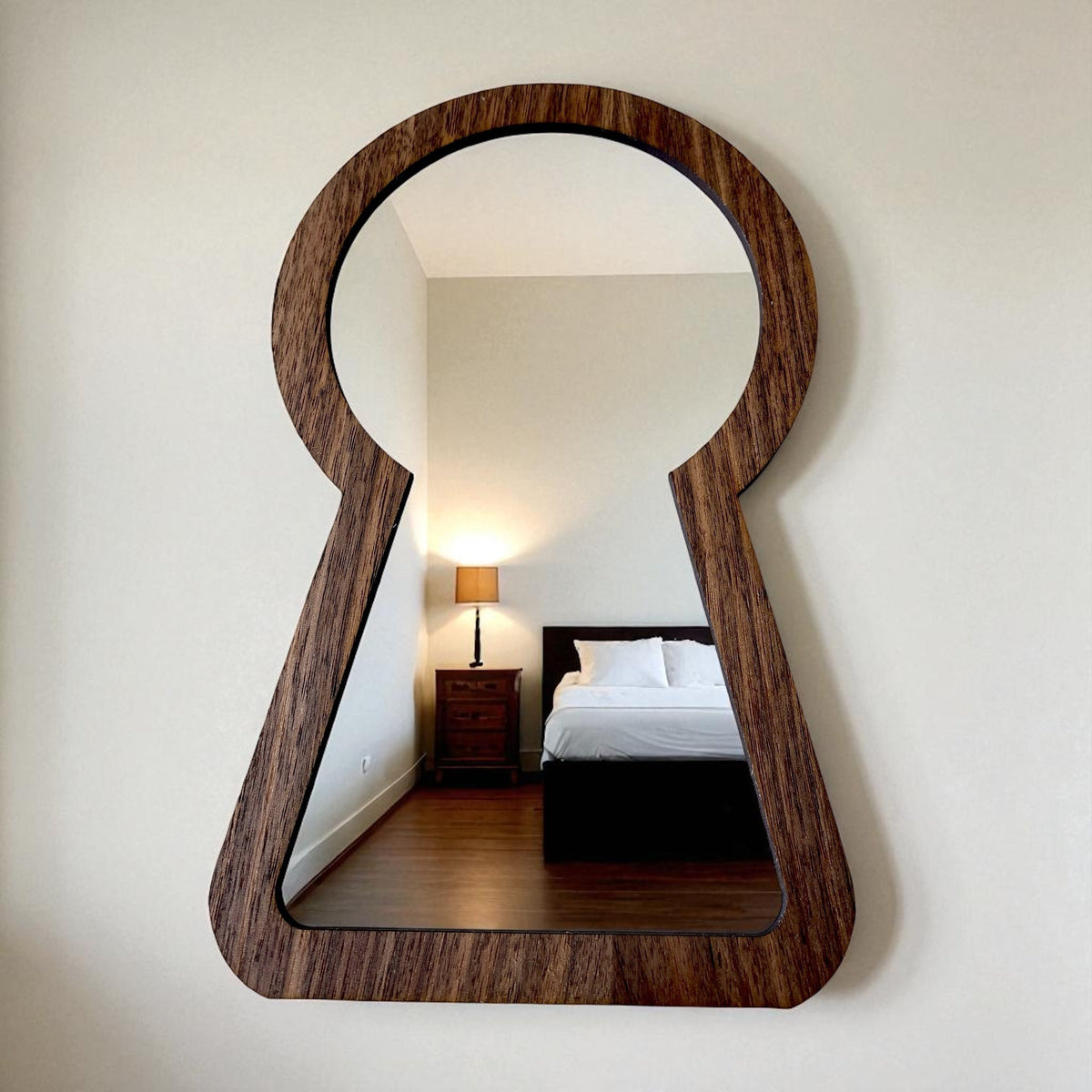 Keyhole-shaped mirror with a brown wood frame hanging on a white wall, reflecting a bedroom interior.
