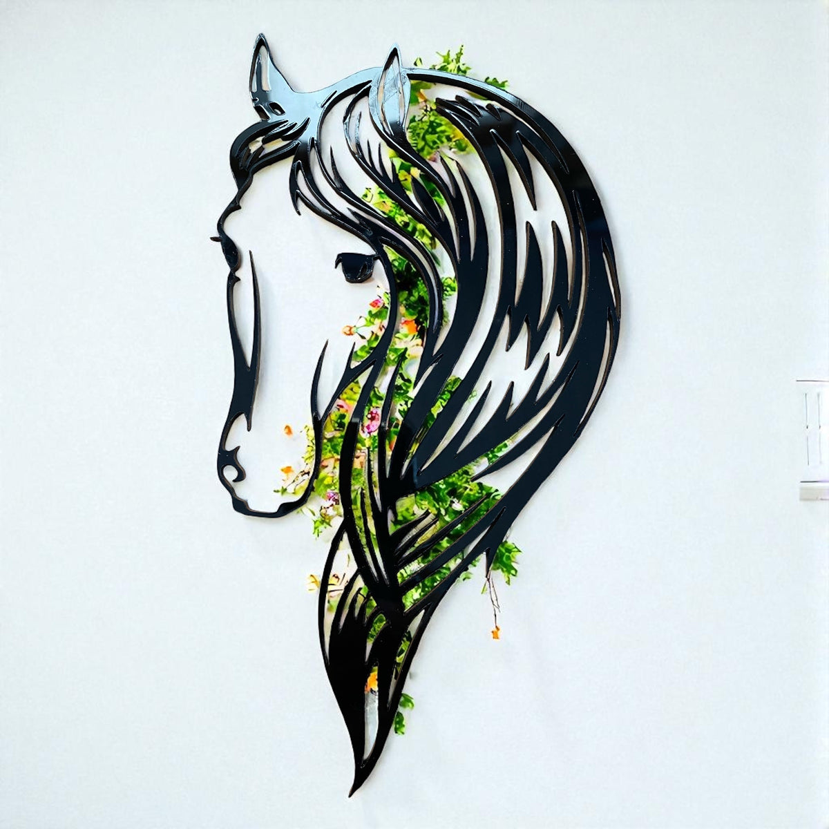 Black metal horse head garden mirror showing reflected green foliage on a wall.