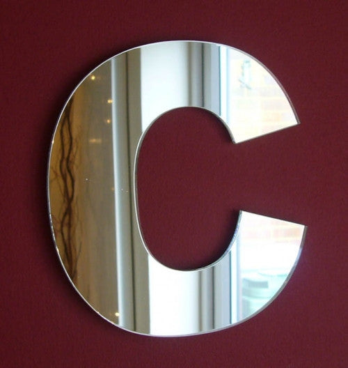 A contemporary mirror shaped like the letter C, mounted on a red wall.