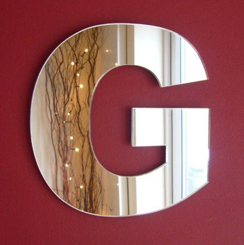 Contemporary letter G mirror mounted on a red wall.