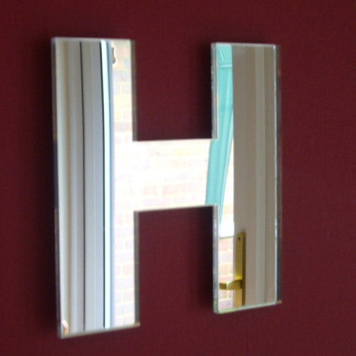 A contemporary mirror shaped like the letter H, mounted on a maroon wall.