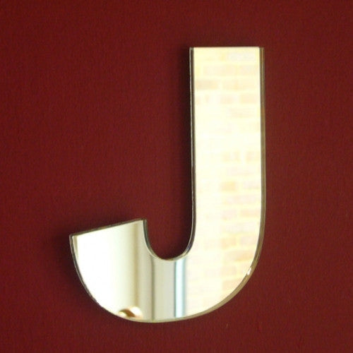 Letter J shaped wall mirror mounted on a solid dark red wall.