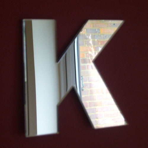 Contemporary letter K shaped mirror mounted on a dark red wall.