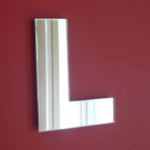 Contemporary letter L mirror hanging on a solid red wall.