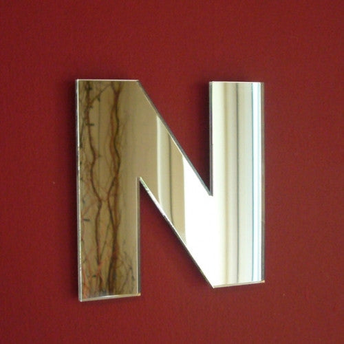 Contemporary letter N shaped mirror hanging on a dark red wall.