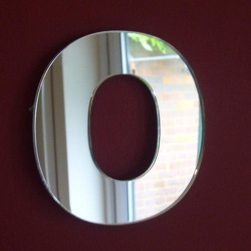 Contemporary letter O-shaped wall mirror mounted on a dark red wall.