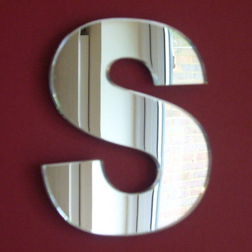 A reflective mirror shaped like the uppercase letter S, mounted on a solid dark red wall.