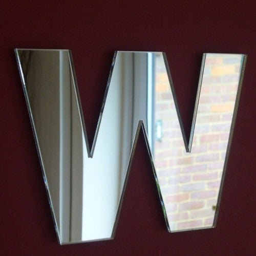 A contemporary wall mirror shaped like the letter W with beveled edges on a dark red wall.