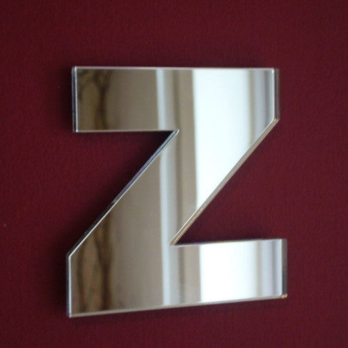A silver mirror in the shape of the letter Z on a dark red wall.