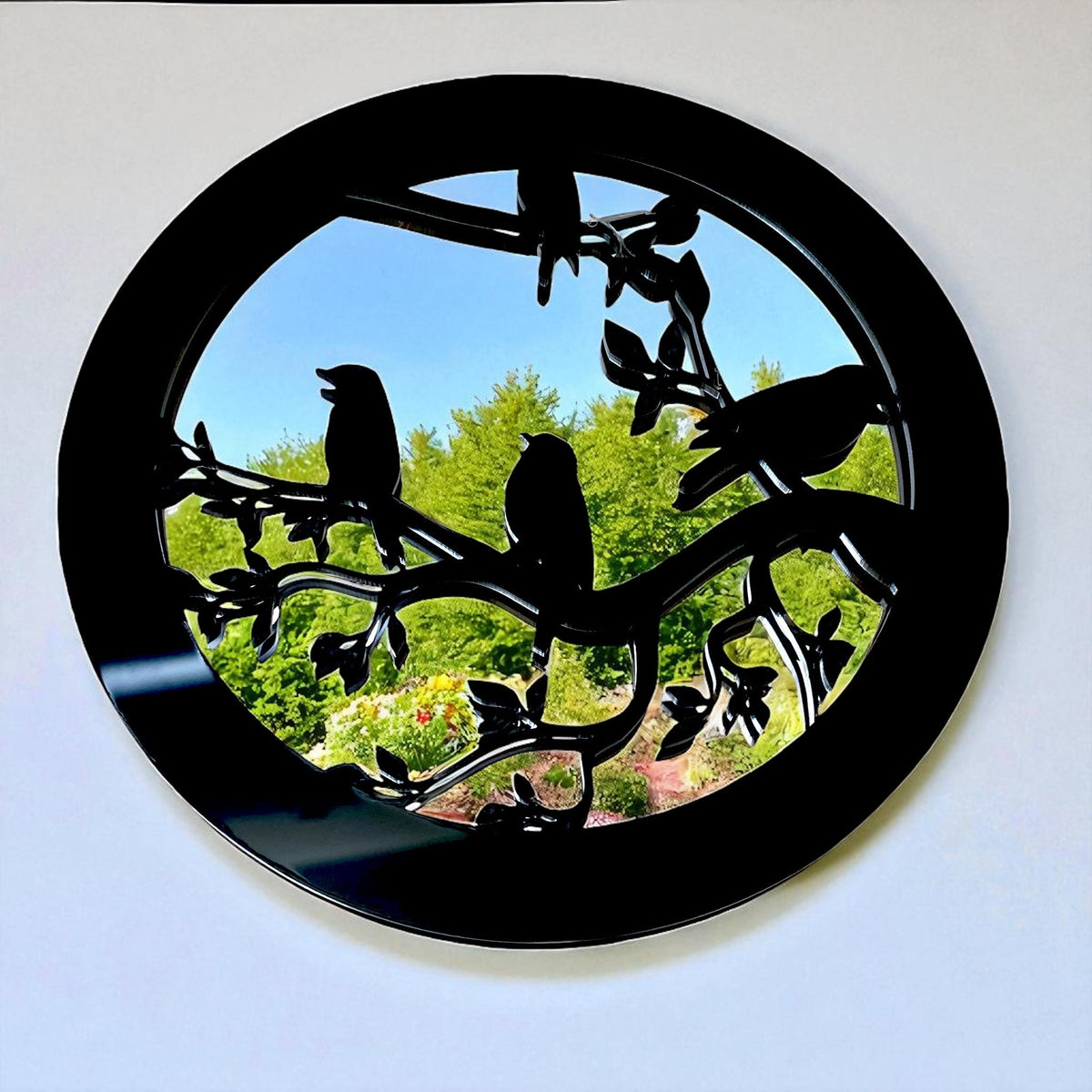 Round black garden mirror featuring silhouette birds perched on a leafy branch overlay.