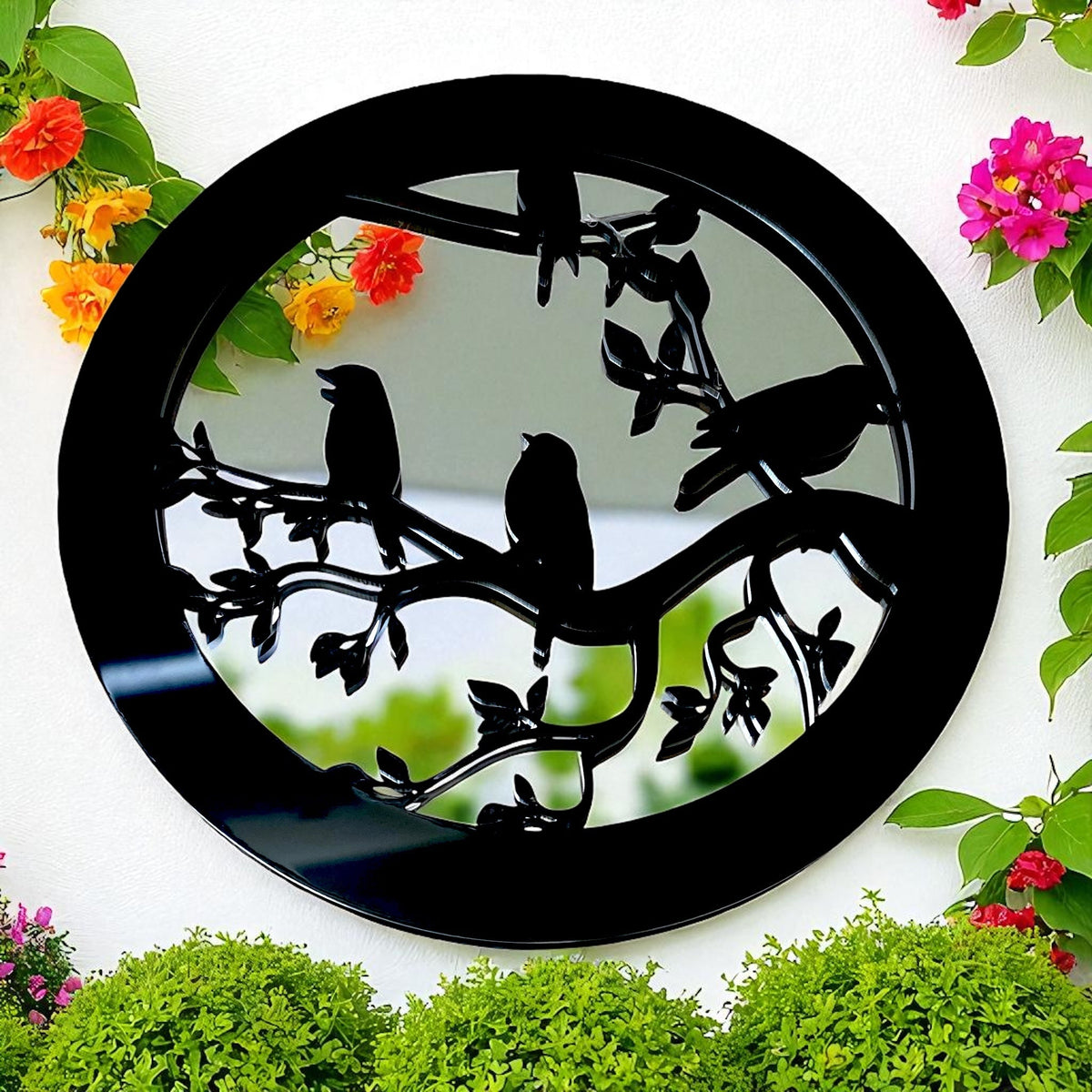 Round black garden mirror featuring silhouette birds and branches, surrounded by flowers.