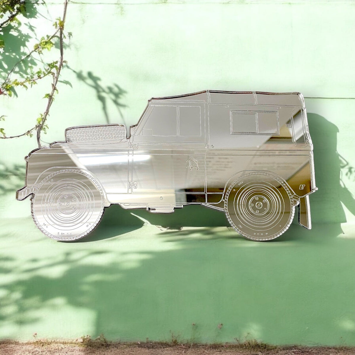 An SUV-shaped reflective mirror with etched details of wheels and windows on a green wall.