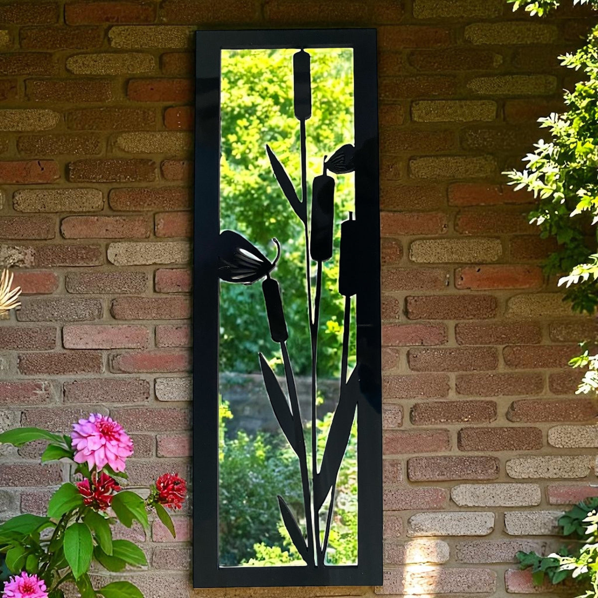 Rectangular black garden mirror with a black metal bulrush and butterfly overlay, hanging on a brick wall.