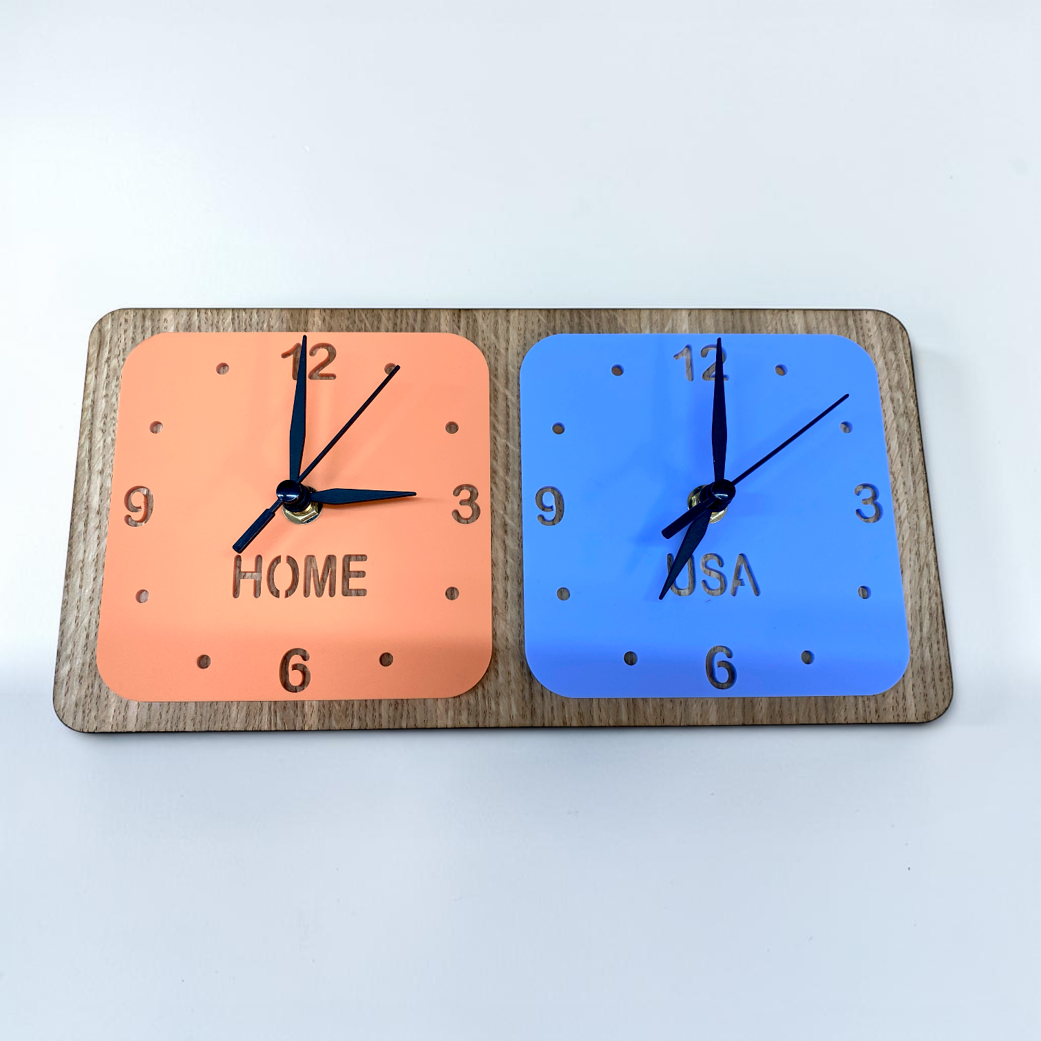 Two square clocks on a wooden stand: one orange labeled "HOME," one blue labeled "USA," both with black hands.