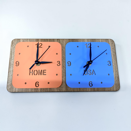Two square clocks on a wooden stand: one orange labeled "HOME," one blue labeled "USA," both with black hands.