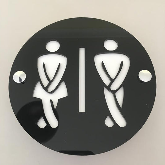 Round black acrylic toilet sign with mirrored cut-out figures of two people with crossed legs and a dividing line.