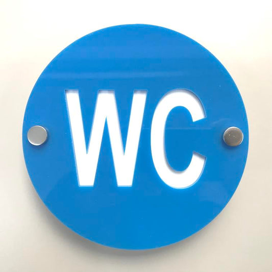 Round blue acrylic toilet sign with cut-out white WC letters and two silver standoffs.