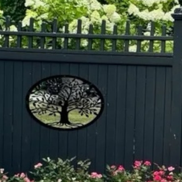 Oval garden mirror featuring a black metal Tree of Life overlay, mounted on a dark fence.
