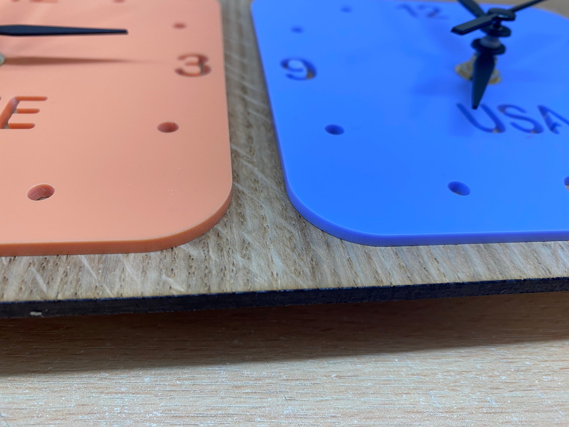 Two square clocks in peach and blue, mounted on wood. Each features black hands and personalized "USA" text.
