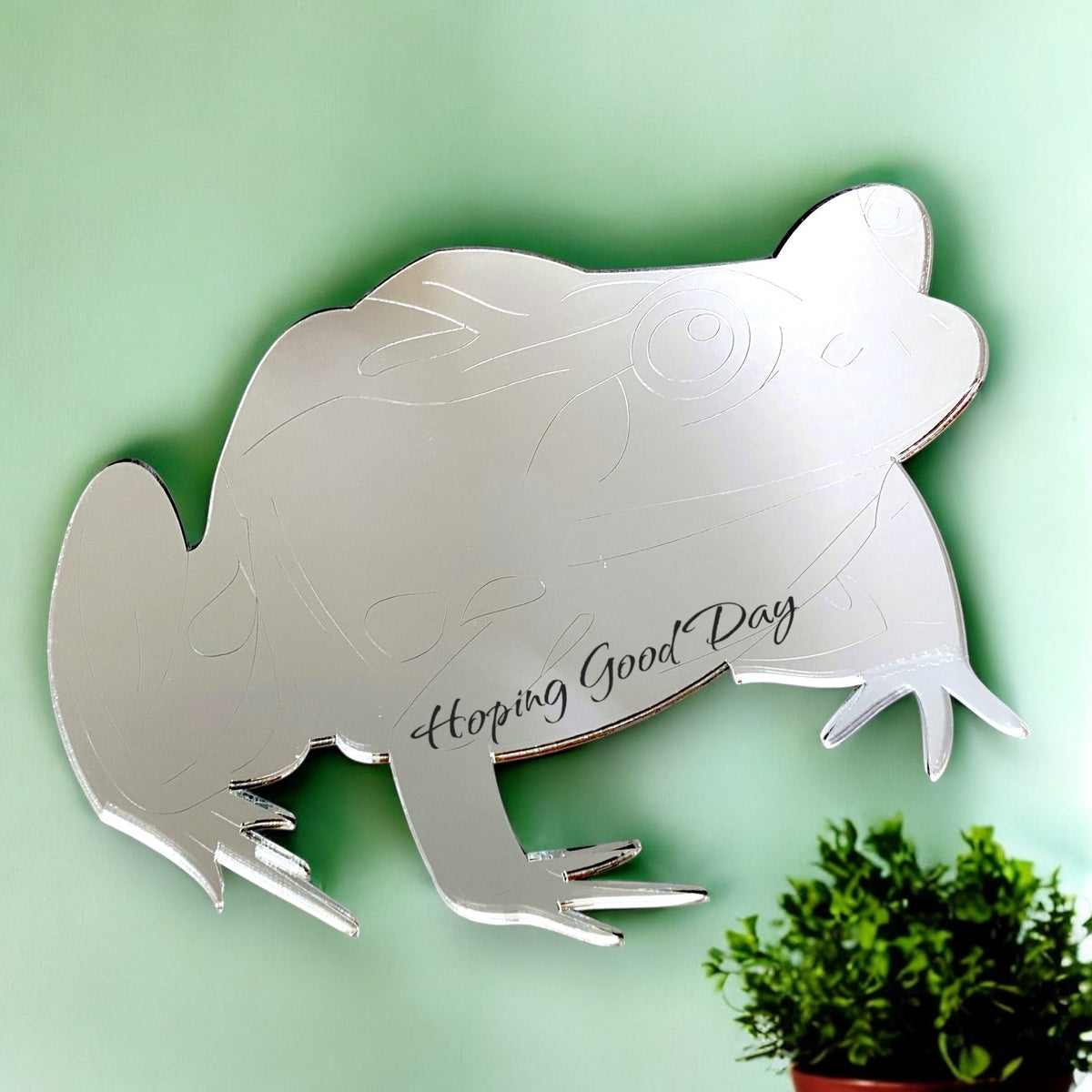 An etched frog-shaped silver mirror with the text "Hoping Good Day" on a light green background.